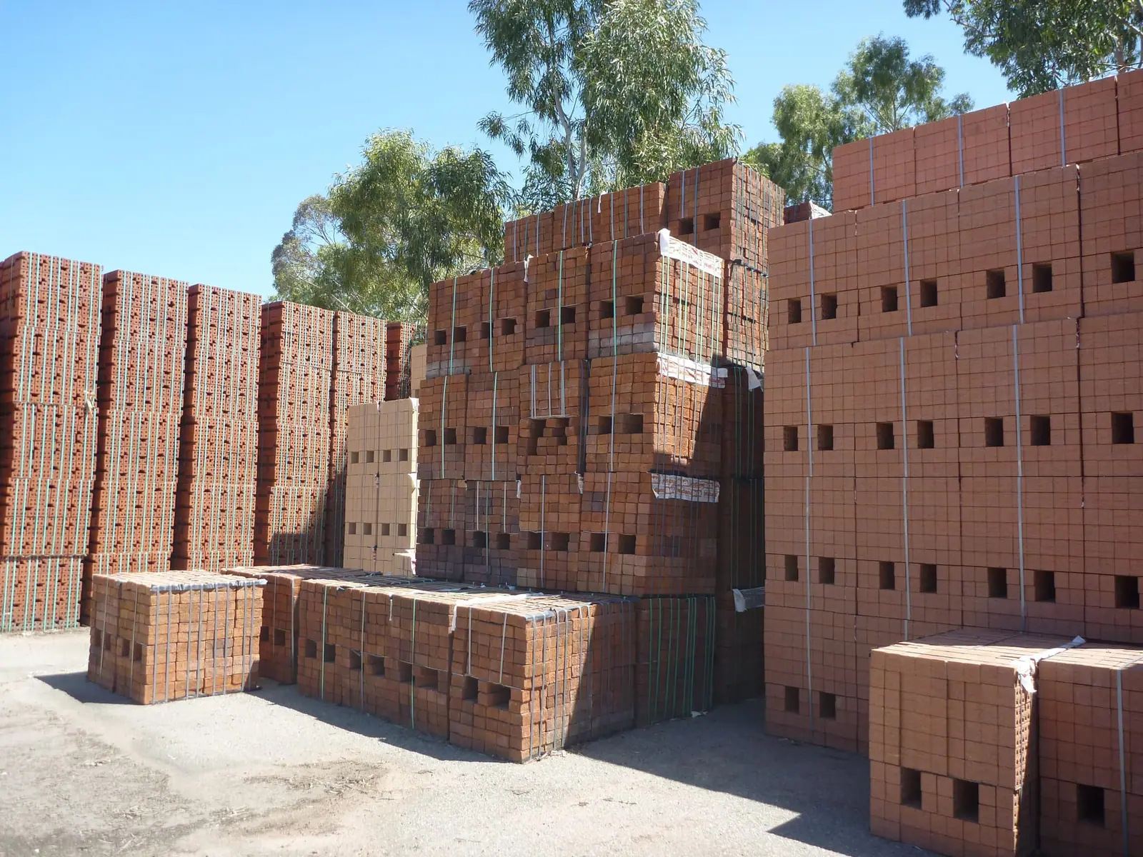 Tall stacks of perforated red building bricks bundled on a brickworks yard