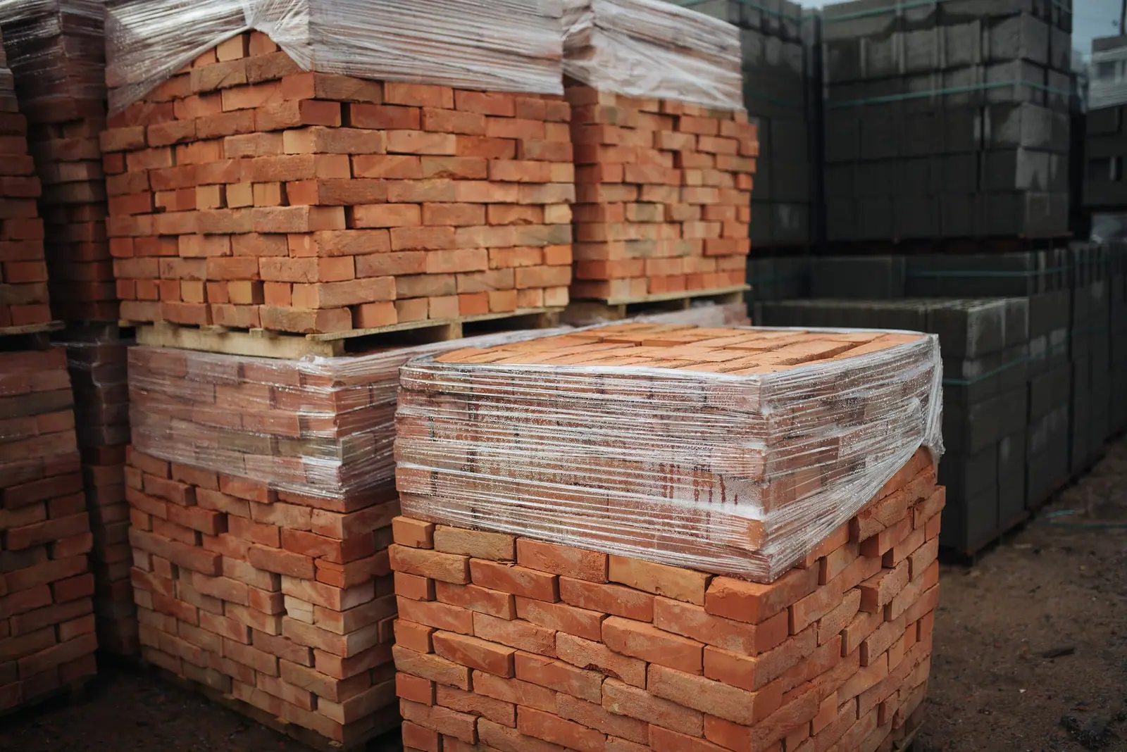Wrapped pallets of red construction bricks stacked beside concrete blocks, ready for supply