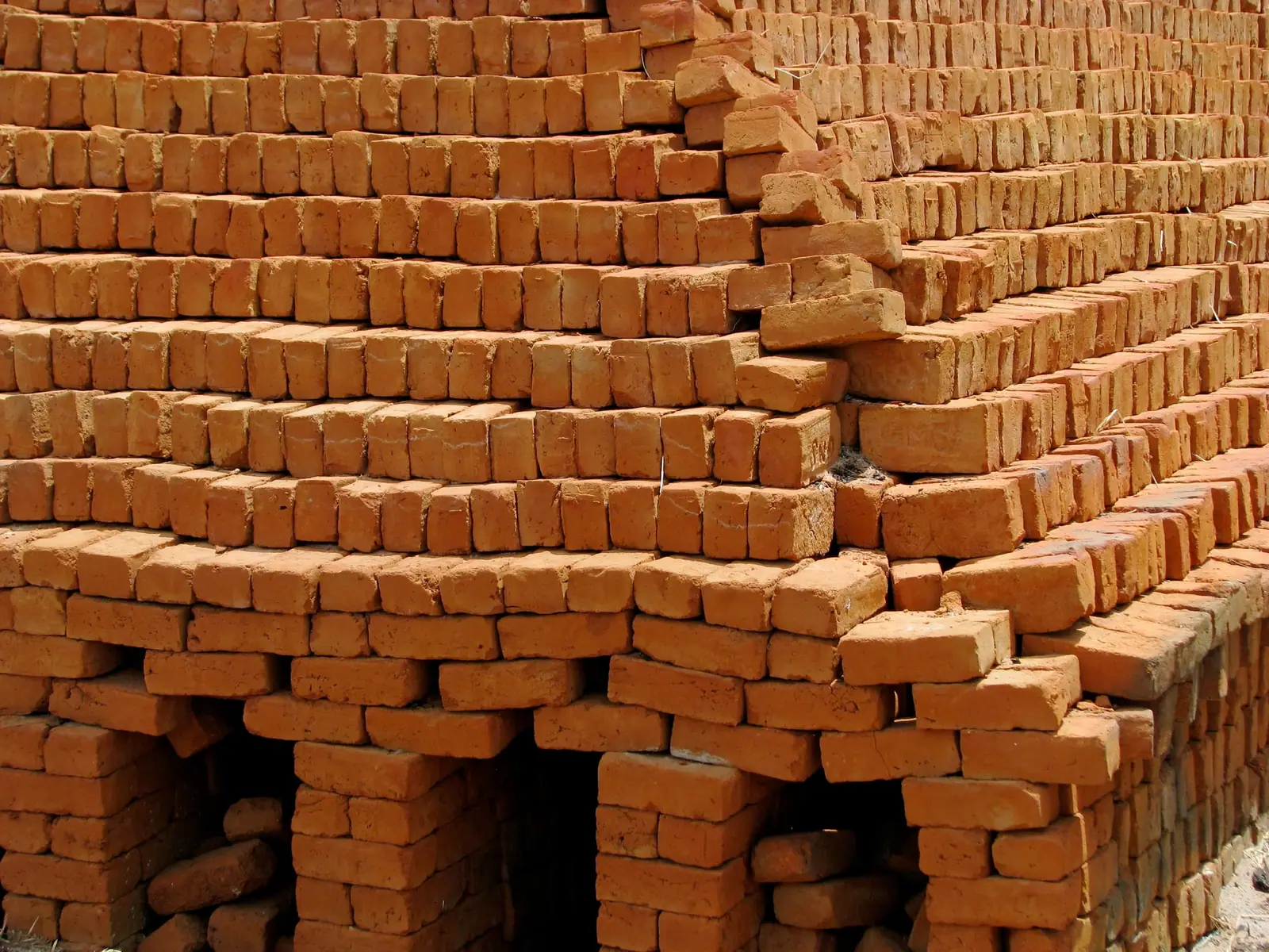 Close view of a large stack of fired red clay bricks with open channels for airflow